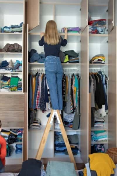 Woman standing on a ladder looking in her messy wardrobe, overwhelmed by mess