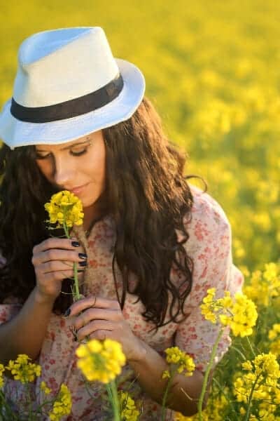 Woman wearing a white hat in a field of yellow flowers, smelling flower