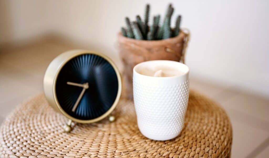 A clock and white candle sitting on a wicker table