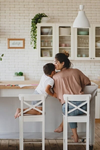 Woman kissing her son on forehead. Both are sitting on high chairs in a kitchen